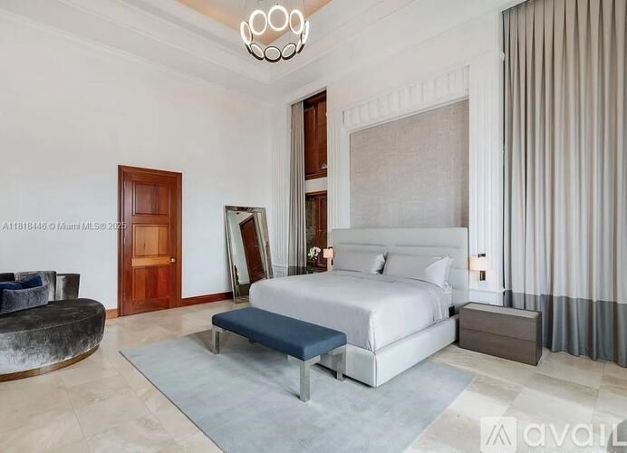 A bedroom with a large bed, a round ottoman, and a chandelier.