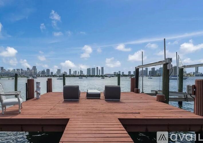A wooden dock with two chairs and a table in the foreground with a city skyline in the background.