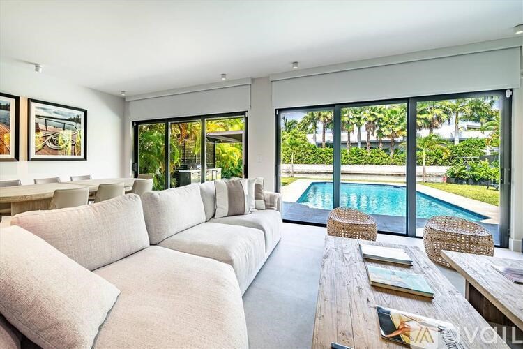 A living room with a large couch and a pool outside the window.