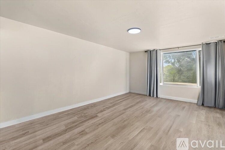 A room with wooden flooring and a window with curtains.