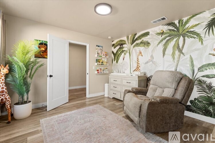 A living room with a giraffe, a chair, and a wallpaper with palm trees.