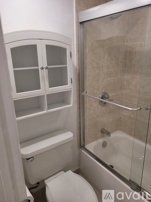 A white bathroom with a toilet, a shower with a glass door, and a cabinet above the toilet.