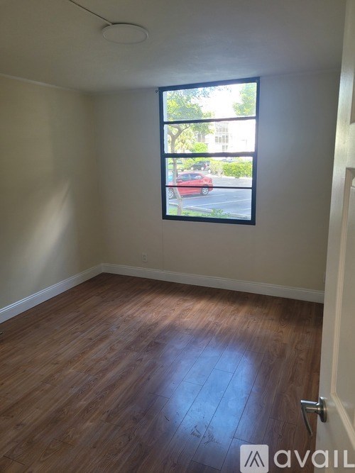 A room with wooden flooring and a window showing a red car and trees outside.