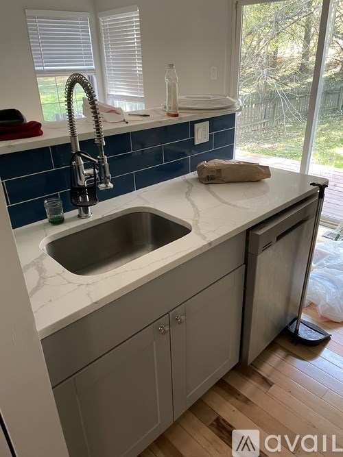 A kitchen with a blue tile backsplash and a stainless steel sink.