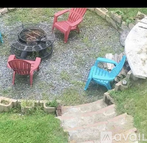 A fire pit surrounded by red and blue chairs in a gravel backyard.