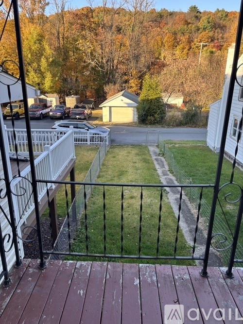 A balcony with a black railing overlooks a green lawn and a parking lot.