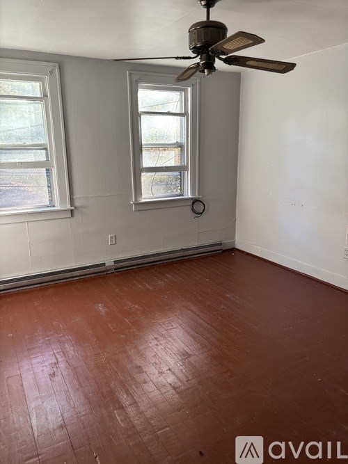 A room with a ceiling fan and two windows.