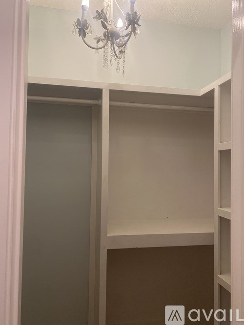 A chandelier hangs over a white closet with brown shelving.