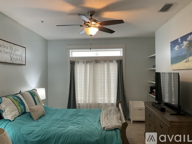 A bedroom with a bed, a ceiling fan, and a painting on the wall.