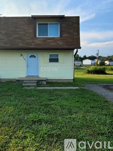 A small house with a blue door and a window is surrounded by a grassy area.