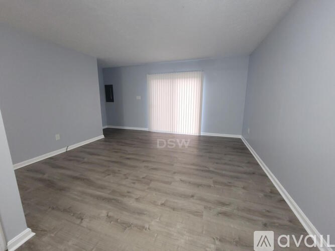 A spacious room with wooden flooring and a window with blinds.