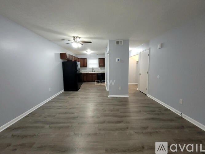 A spacious empty room with a black refrigerator and wooden flooring.