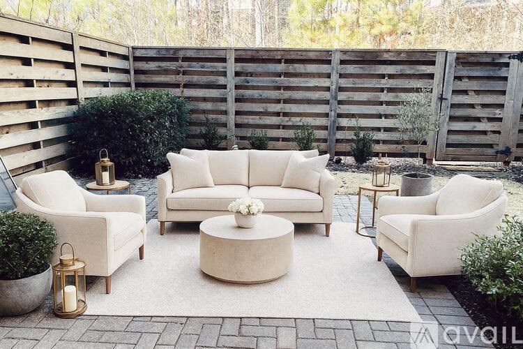A white couch and chairs are arranged on a rug in a backyard.