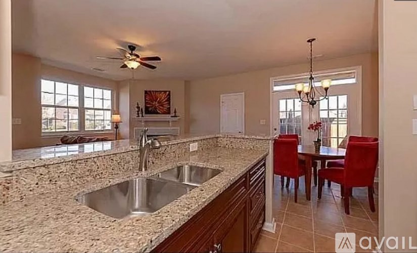 A kitchen with granite countertops and a dining area with red chairs.
