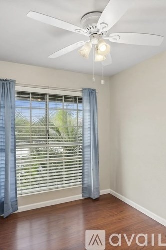 A room with a ceiling fan and a window with curtains.