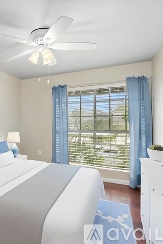 A bedroom with a bed, a ceiling fan, and a window with blue curtains.