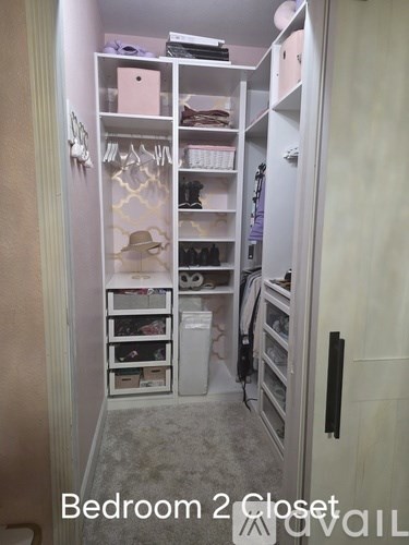 A small closet with a white door and a white shelf with a pink box on it.
