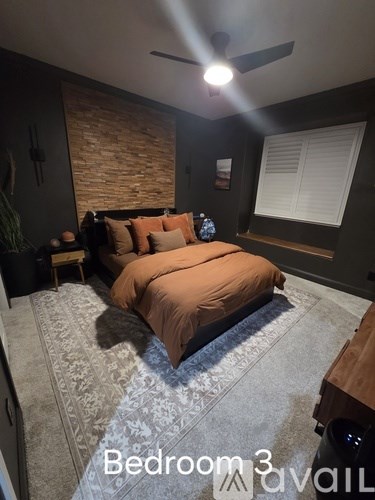 A bedroom with a bed, a ceiling fan, and a brick wall.