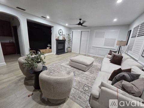 A living room with a grey sofa, a round ottoman, and a black fireplace.