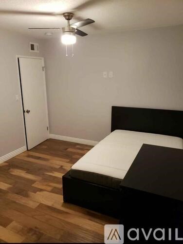 A bedroom with a bed, wooden floors, and a ceiling fan.