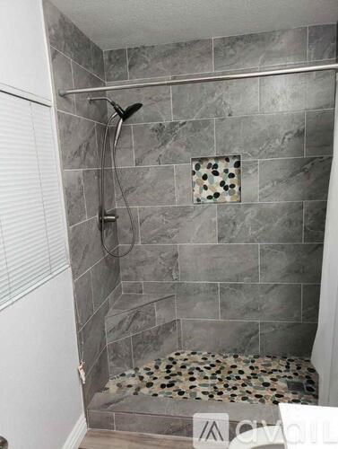 A shower area with a grey tile wall and a shower head.