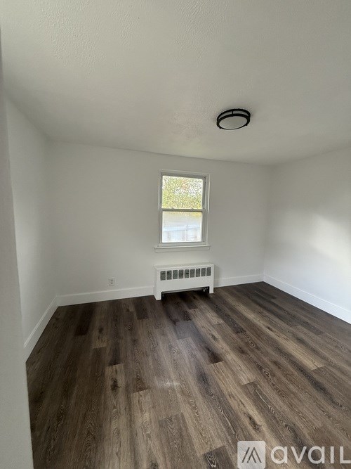 A room with wooden flooring and a window with a white radiator beneath it.