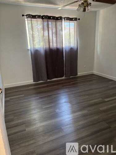 A room with wooden flooring and a window with curtains.