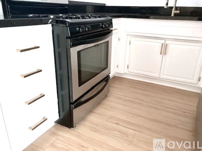 A black stove top oven with a glass door sits in a kitchen with white cabinets and a wooden floor.