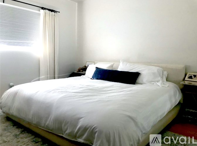 A bed with white sheets and a white headboard with a blue pillow on it.