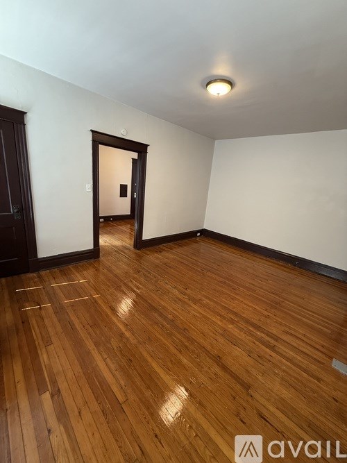 A room with wooden flooring and a doorway leading to another room.