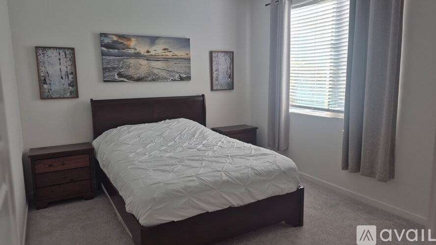 A bedroom with a bed, two pictures on the wall, and a window with curtains.