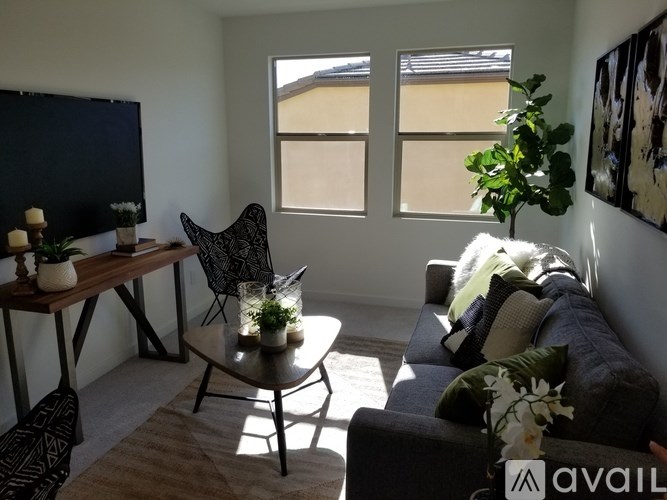 A living room with a grey couch, a black chair, a wooden table with candles and plants on it, and a painting on the wall.