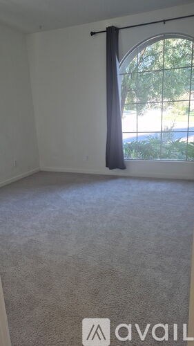 A room with a carpeted floor and a window with a curtain.