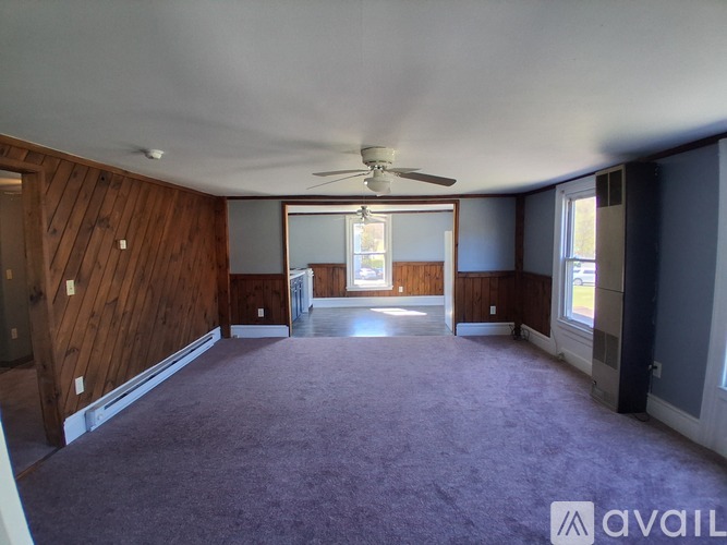 A spacious room with a ceiling fan and purple carpeting.