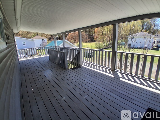 A wooden deck with a railing and a view of a house and trees.