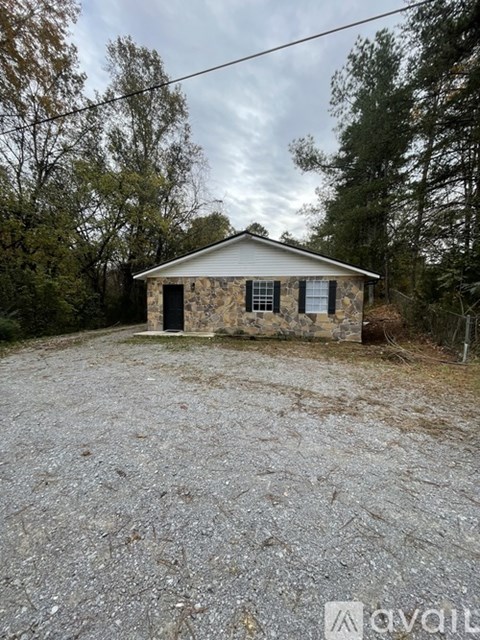 A small stone house with a gravel driveway in front of it.