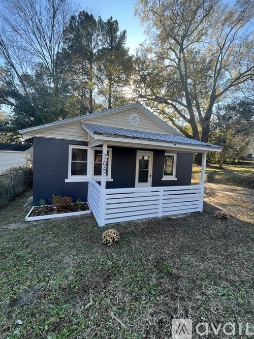 A small house with a grey roof and white trim is surrounded by a grassy area.