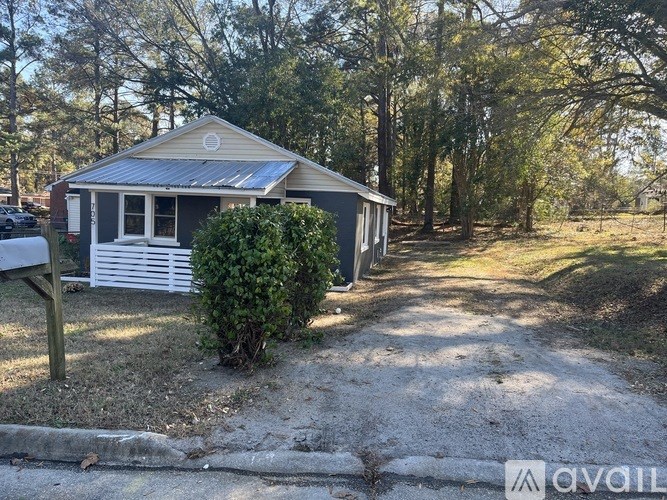 A small house with a grey roof and a white fence is surrounded by trees.