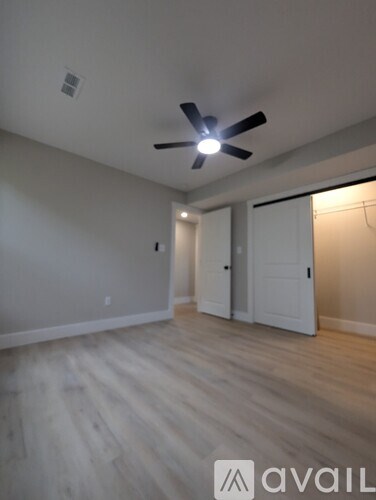 A room with a ceiling fan and light, wooden floors, and a white door.