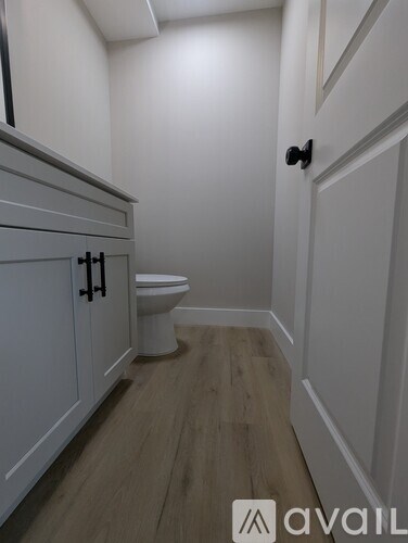 A white toilet sits in a small bathroom with wood flooring and white walls.