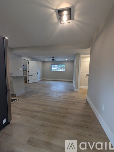 A spacious room with wooden flooring and a refrigerator on the left side.