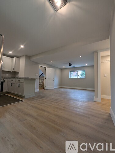 A spacious room with wooden flooring and a kitchen area in the background.