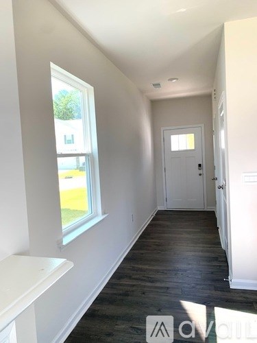 A hallway with a white door and a window with a view of a green lawn.