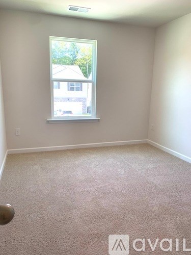 A room with a carpeted floor and a window showing a view of a house.