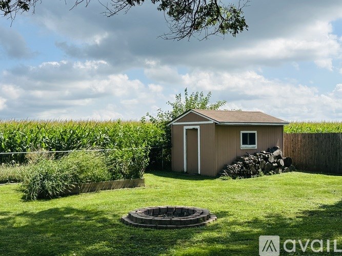 A small house with a brown roof is surrounded by a grassy area and a pile of wood.