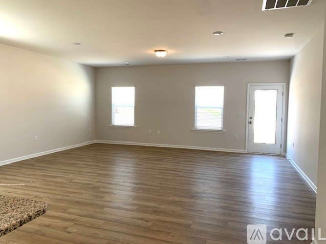 A spacious room with wooden flooring and two windows.