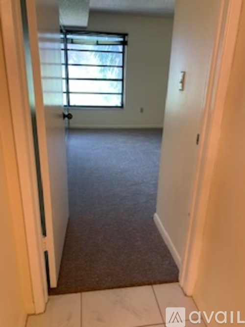 A hallway with a carpeted floor and a window with blinds.
