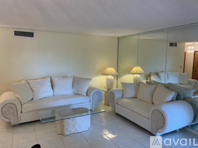 Two white couches with pillows and a glass table in a room.