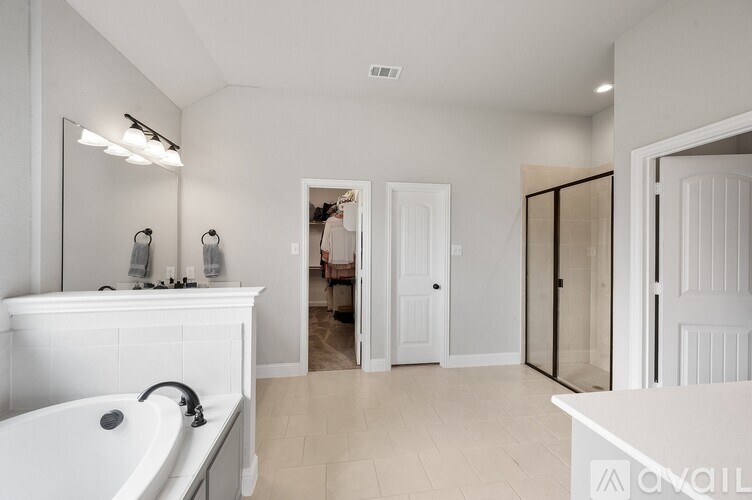 A white bathroom with a tub, sink, mirror, and a doorway leading to another room.
