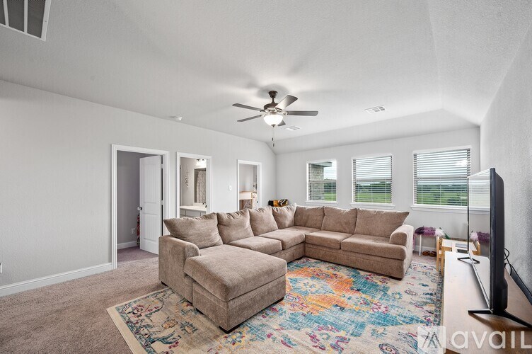 A living room with a beige couch and a rug with a television on the right side.